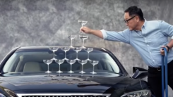 Akio Toyoda builds a tower of champagne glasses on the hood of a Lexus LS 500