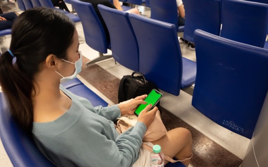 Thai lady texting on the phone at the airport. Asian girl use a protection mask for coronavirus or covid 19 in airport. - stock image