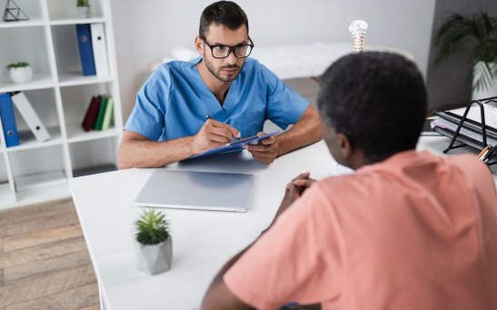 young doctor writing clipboard while listening mature african american patient