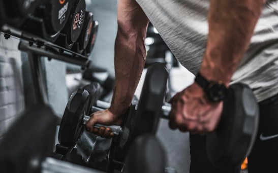 person in gray shirt holding black dumbbell